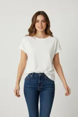 Remera blanca de algodón con lavado, corte holgado y cuello redondo a la base. Las mangas son cortas y tienen el borde doblado hacia afuera.