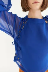 Blusa azul de crepe con transparencias y mangas largas abullonadas. Presenta detalle de lazos en los hombros y laterales.