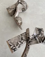 Sandalia de taco cuadrado alto, con diseño de punta cuadrada, tira delantera ancha y tira ajustable en el tobillo con hebilla metálica.