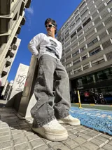 Pantalón de jean con corte baggy y diseño balloon, de color gris lavado con efecto desgastado. Presenta costuras laterales curvadas y una silueta amplia y holgada.