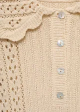 Jersey de punto calado en color beige, con diseño de manga corta, cuello polo con terminación en ondas y cierre frontal de botones.