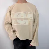 Buzo de algodón rústico color beige con corte boxy, cuello redondo y estampa frontal con letras grandes. Presenta costuras decorativas en color blanco y terminaciones desflecadas en el ruedo y puños.