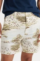 Bermuda de corte clásico con estampado tropical de palmeras y paisajes en tonos tierra sobre fondo beige. Cuenta con cierre de botón y cremallera, bolsillos laterales y bolsillos traseros.