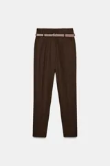 Pantalón de vestir color marrón, de corte recto y largo tobillero. Presenta tiro medio, bolsillos laterales y cierre frontal con cremallera, botón y gancho. Incluye un cinturón fino a tono con hebilla metálica.