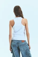 Musculosa de morley color blanco, con cuello alto y diseño de espalda nadadora. Presenta un isologo frontal bordado con tachas brillantes.