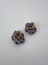 Aros de acero quirúrgico dorados con dijes colgantes en forma de flor translúcida de color lila con lunares negros.