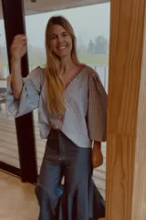 Camisa de rayas azules y blancas, de corte holgado con mangas abullonadas, escote en V y detalle de bordado rojo alrededor del cuello.