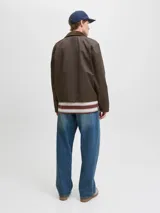 Campera de estilo worker color marrón, con cuello camisero de pana, cierre frontal con cremallera y bolsillos frontales con solapa y broches a presión. Presenta un acabado recubierto que le otorga una textura sutilmente brillante y resistente.