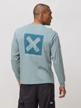 Remera de manga larga en color verde azulado, con corte regular fit. Presenta un estampado cuadrado en la espalda con una X grande y detalles de marca en la manga.