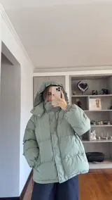 Campera puffer de corte holgado en color beige, con diseño acolchado, cuello alto y capucha desmontable. Cuenta con cierre frontal y botones a presión, además de puños elásticos.