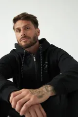 Campera de felpa negra con capucha y cordón ajustable, cierre frontal con cremallera, bolsillos laterales y logo estampado en el pecho.