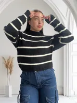 Sweater de punto grueso negro con rayas horizontales blancas, cuello alto y corte holgado.