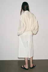 Chaqueta bomber de cuello subido y manga larga, con acabado satinado en color beige. Presenta pliegues frontales, bolsillos laterales ocultos en costura y cierres elásticos en puños y cintura. Cierre frontal con cremallera.