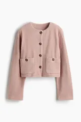 Chaqueta corta de velour acanalado color rosado, con cuello redondo, cierre frontal de botones marrones y dos bolsillos de parche con botón en la parte delantera. Presenta hombros caídos y mangas largas.