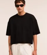 Remera negra de algodón con corte oversized, cuello redondo y manga corta. Presenta un tejido acanalado y un dobladillo sin rematar.