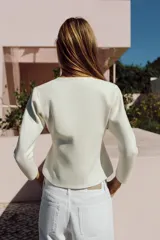 Chaqueta de punto color negro con escote en V, mangas largas y cierre frontal con botones dorados. Presenta un diseño de bajo asimétrico.
