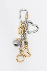 Llavero metálico combinado en tonos plateado y dorado, con mosquetón superior, dijes en forma de corazón, cadena de eslabones y esfera con grabado.