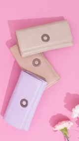 Billetera larga de símil cuero color marrón claro, con solapa frontal decorada con un aro metálico central. Cuenta con múltiples compartimentos internos para tarjetas, billetes y un monedero con cierre.