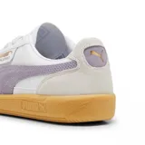 Championes Puma modelo Palermo LTH, con diseño de perfil bajo, cuerpo de cuero blanco, detalles en gamuza gris y franja lateral en color lila. Cuenta con suela de goma color caramelo y logo dorado en el lateral.