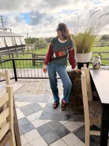 Sweater de punto color verde oscuro con detalles bordados a mano en tonos naranja, marrón, blanco y rojo. Presenta cuello redondo y mangas largas.