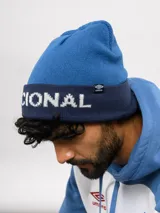 Gorro tipo beanie de punto color azul, con el nombre del Club Nacional de Football tejido en letras blancas y una franja decorativa en tono azul oscuro.