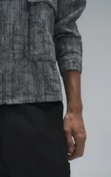 Campera de denim rígido con diseño de trama texturizada en tonos grises y negros. Presenta cuello camisero, cierre frontal con botones, mangas largas y dos bolsillos frontales con solapa.