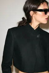 Blazer corto de lino color beige, con cuello redondo y cierre frontal cruzado con un botón negro.