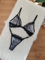 Conjunto de lencería compuesto por corpiño triangular y bombacha tipo tanga. El diseño combina microtul con estampado animal print y detalles de encaje negro en los bordes. El corpiño cuenta con cierre frontal y breteles regulables.
