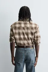 Camisa de corte relajado confeccionada en tejido de algodón con estampado de cuadros en tonos marrones y beige. Presenta cuello solapa, manga larga con puños abotonados, bolsillo plastrón en el pecho y cierre frontal con botones.