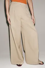 Pantalón de tiro medio confeccionado en hilatura de algodón, de corte wide leg y pernera ancha. Presenta cintura con trabillas, bolsillos laterales ocultos en costura, detalle de pliegues en la parte delantera y cierre frontal con cremallera, botón y ganchos metálicos.