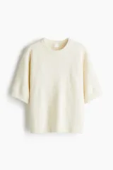Remera de corte holgado en tejido de punto suave, color blanco, con hombros caídos, mangas al codo y ribetes acanalados en el cuello, puños y dobladillo.
