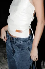 Top de cuero color blanco, de diseño halter con cuello alto y espalda descubierta con tiras ajustables laterales.