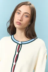 Cardigan de algodón color crudo, de corte corto y ajuste frontal con botones. Presenta detalles de ribetes a contraste en cuello, puños y ruedo, con una estética clásica y versátil.