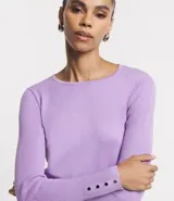 Suéter de punto color rosado, con cuello barco, mangas largas y puños con botones decorativos. El dobladillo también es acanalado.