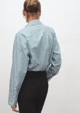 Camisa de popelín de algodón orgánico con diseño oversize, cuello camisero, manga larga con puños abotonados y cierre frontal de botones.