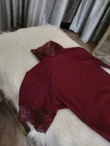 Body de lycra color bordó con cuello alto, mangas cortas y espalda descubierta. Presenta detalles de encaje en el cuello, mangas y laterales de la parte inferior. Cuenta con cierre de broches en la entrepierna.