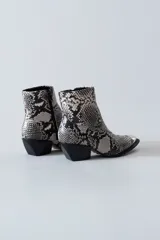 Bota texana corta con estampado de piel de serpiente en tonos blanco y negro, puntera metálica plateada, cierre lateral y taco bajo.