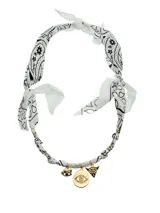 Collar tipo bandana de tela blanca con estampado de cachemira en negro, atada al cuello y adornada con dijes dorados de ojo turco, ojo con pestañas y pirámide con ojo.