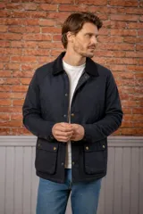 Campera encerada de estilo clásico con cuello de pana, cierre frontal con cremallera y botones a presión, y bolsillos frontales con solapa.