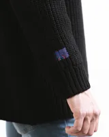 Sweater negro de punto con cuello redondo y corte holgado. Diseño con motivo de zurcido en la manga izquierda.