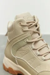 Zapatilla tipo hiking de caña media, confeccionada en una combinación de símil cuero y nylon en tonos beige y rosa suave. Presenta cordones al tono, interior acolchado para mayor abrigo y suela de goma dentada en color marrón con entresuela gris.