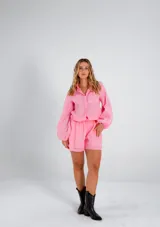Conjunto de dos piezas compuesto por una camisa de corte relajado con mangas largas abullonadas y puños elásticos, y un short de tiro medio con cintura elástica y diseño de doble ruedo. Confeccionado en lino liviano.