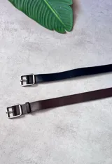 Pack de dos cinturones delgados de cuero liso, uno negro y otro marrón oscuro, ambos con hebilla metálica rectangular plateada.