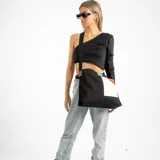 Bolso tote de lona negra con diseño geométrico en blanco, azul claro y marrón. Tiene una correa ajustable de tela negra y detalles de cuero marrón.