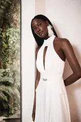 Vestido largo blanco de raso con cuello halter, abertura en el busto, pliegues, falda superpuesta y cremallera invisible en la espalda.