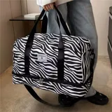 Bolso deportivo de viaje marca Zuomanni, con estampado animal print de leopardo en blanco y negro. Cuenta con doble asa de mano, correa de hombro ajustable y extraíble, y un compartimento inferior independiente con cierre.