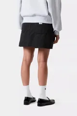 Minifalda negra de lona de algodón con lavado a la piedra, corte recto y cintura alta. Presenta detalles de costuras reforzadas, bolsillos delanteros redondeados estilo utilitario con remaches metálicos y una etiqueta cuadrada tejida en la parte trasera.