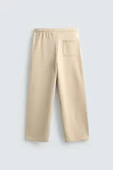 Pantalón jogger de corte relajado y pernera ancha, confeccionado en tejido de algodón con interior perchado. Cuenta con cintura elástica ajustable mediante cordón interior, bolsillos laterales y un bolsillo trasero de plastrón.