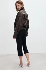 Cazadora tipo biker de cuero sintético en color marrón oscuro, con cuello subido, cierre frontal cruzado con botones forrados y cremallera oculta. Presenta mangas largas con trabillas en los hombros, bolsillos laterales de vivo y bajo con acabado elástico.