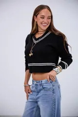 Sweater corto de punto trenzado en color negro, con cuello en V y detalles de rayas blancas en el cuello, puños y ruedo. De manga larga y ajuste cropped.